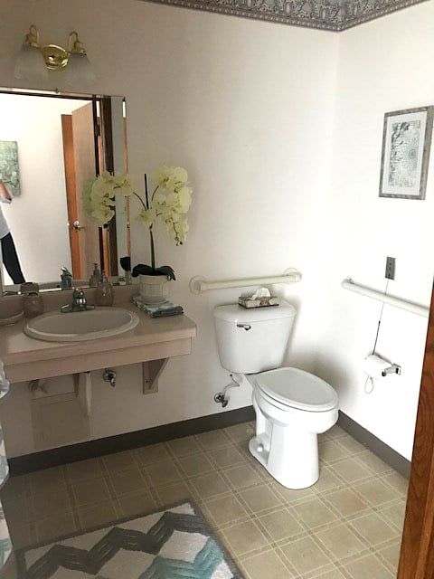 A clean bathroom with a toilet, sink, mirror, and decorative flowers.
