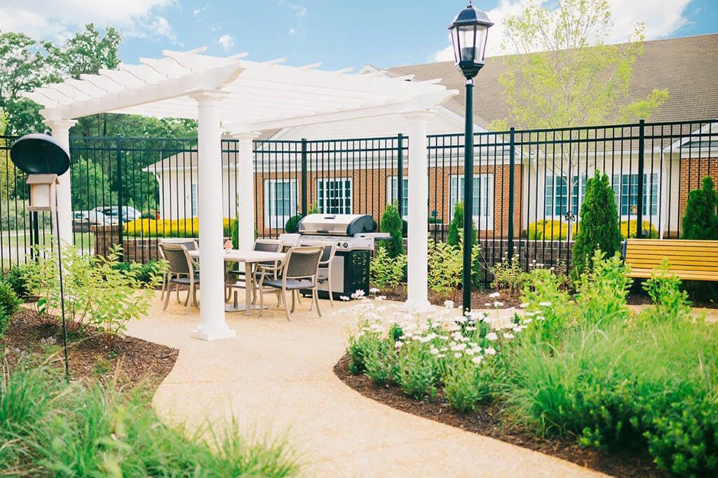 A beautifully landscaped patio area with a pergola, outdoor seating, and a grill.