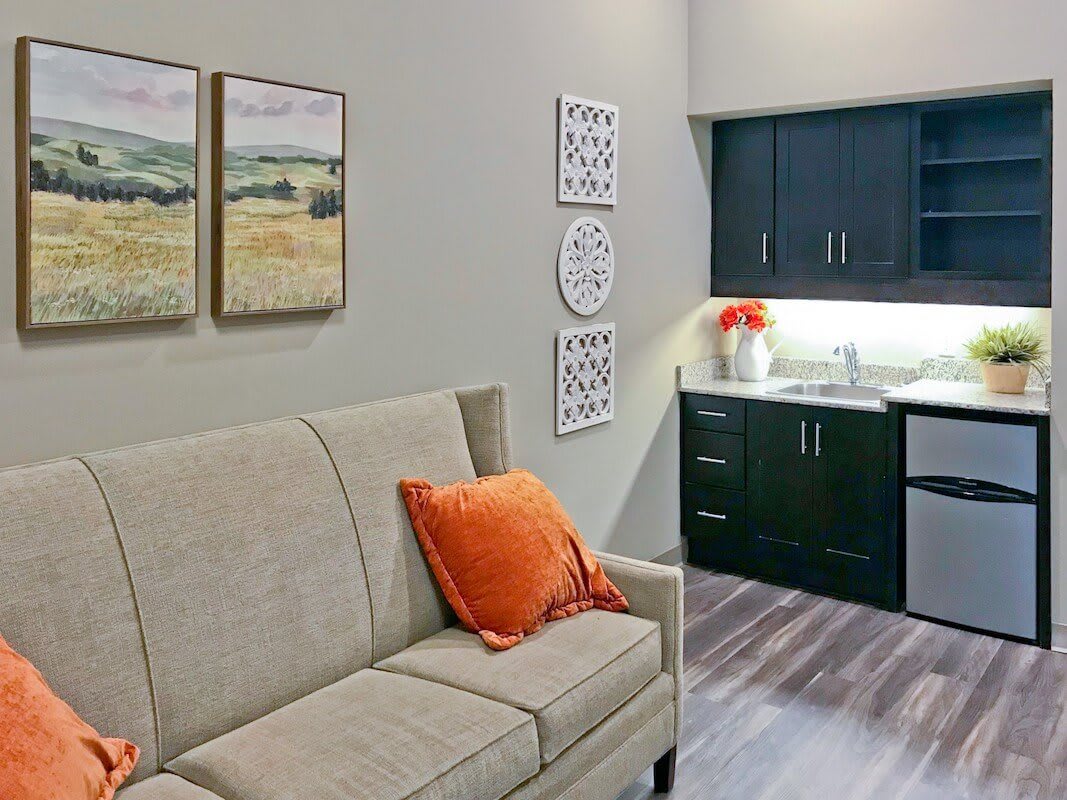 A cozy living area with a beige sofa, orange cushion, and adjacent kitchenette.