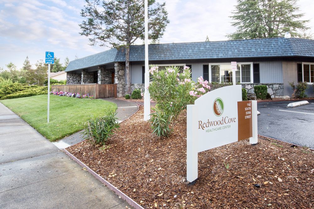 A welcoming entrance to a building surrounded by well-maintained landscaping with a prominent sign in the front.