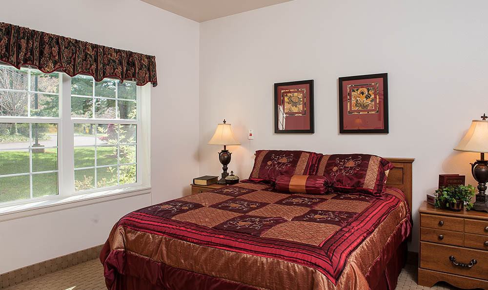A cozy bedroom with a bed, decorative pillows, artwork on the walls, a lamp, and a window.