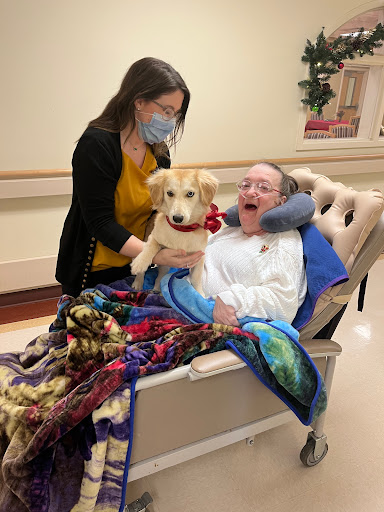 A heartwarming moment in a hospital setting as a caregiver shares a joyful interaction with a patient and a therapy dog, bringing comfort and smiles.