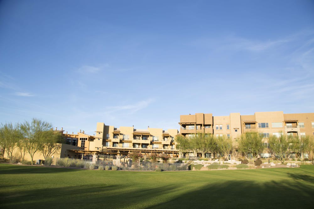 A modern building set against a clear blue sky with a grassy field in the foreground.