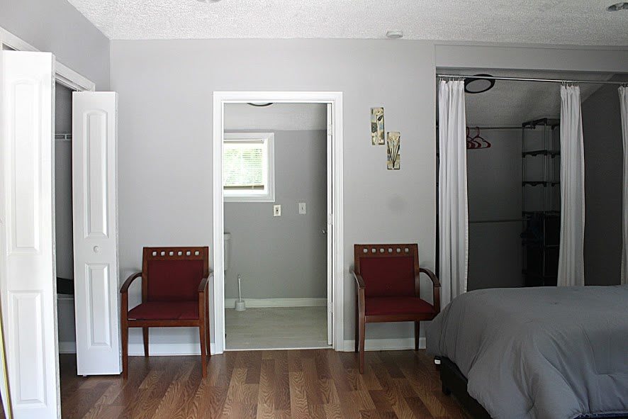 A bedroom interior with two chairs, a bed, and a wooden floor.
