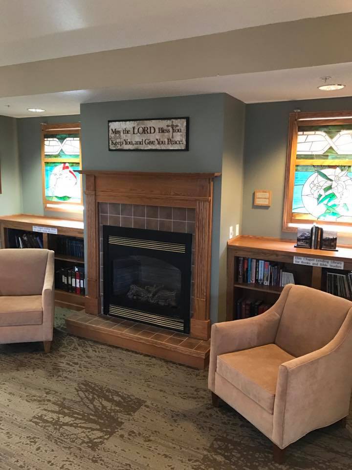 A cozy living room featuring a fireplace, two armchairs, stained glass windows, and built-in bookshelves.