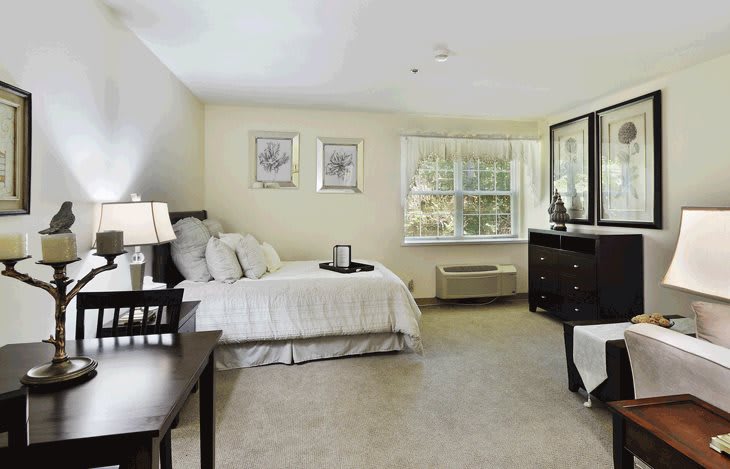 A spacious bedroom with neutral tones, featuring a comfortable bed, dresser, and large window.