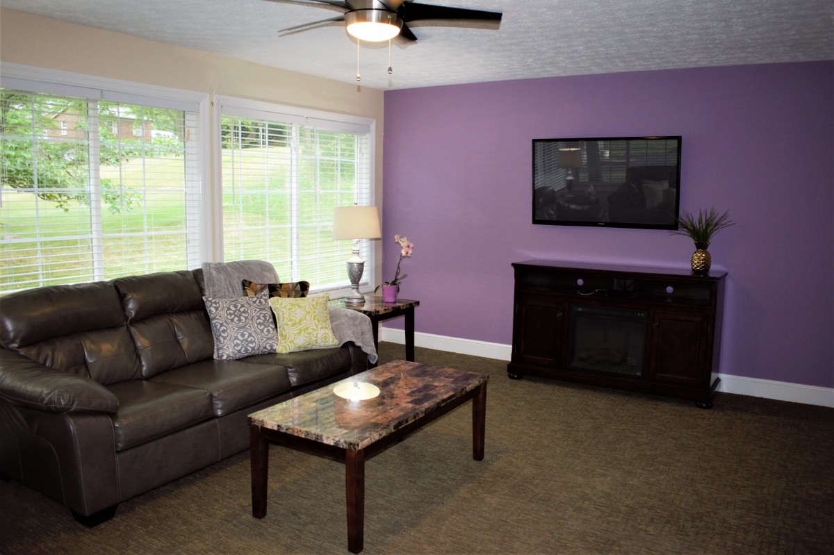 A modern living room with a purple accent wall, sofa, and flat-screen TV.