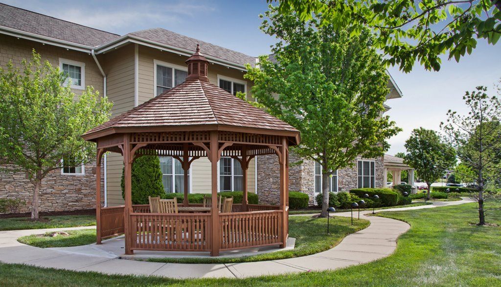 A wooden gazebo surrounded by a landscaped lawn and trees, with a house in the background.