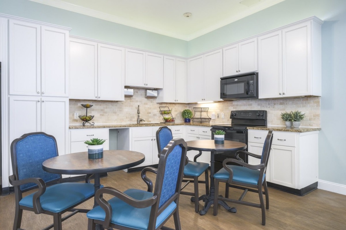 A modern kitchen with white cabinets and blue upholstered dining chairs.