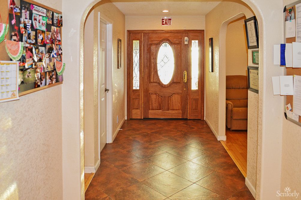 A spacious hallway featuring a wooden front door with glass panels, arched doorways, and tiled flooring.