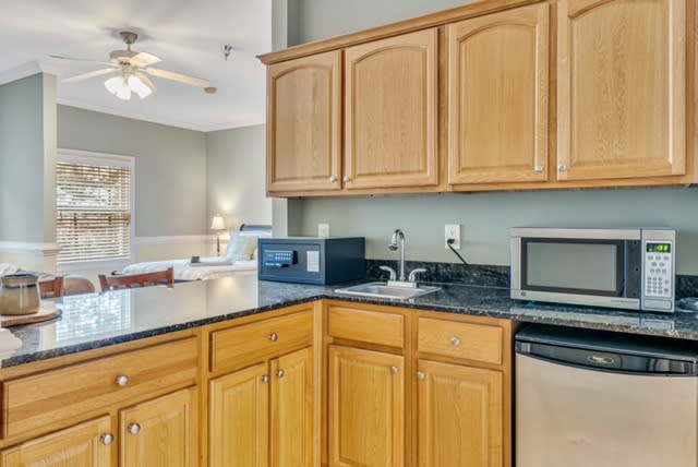 A modern kitchen with wooden cabinets and a black countertop, featuring a microwave and sink.