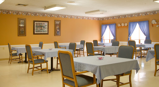 A spacious dining area with neatly arranged tables and chairs, featuring warm orange walls and blue curtains.