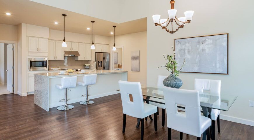 A modern open-plan dining and kitchen area featuring white furniture and elegant lighting.