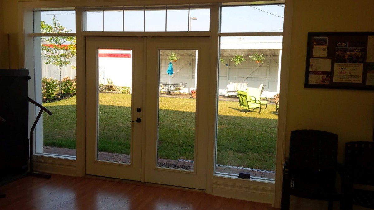 View of a backyard through French doors, featuring a lawn and outdoor furniture.