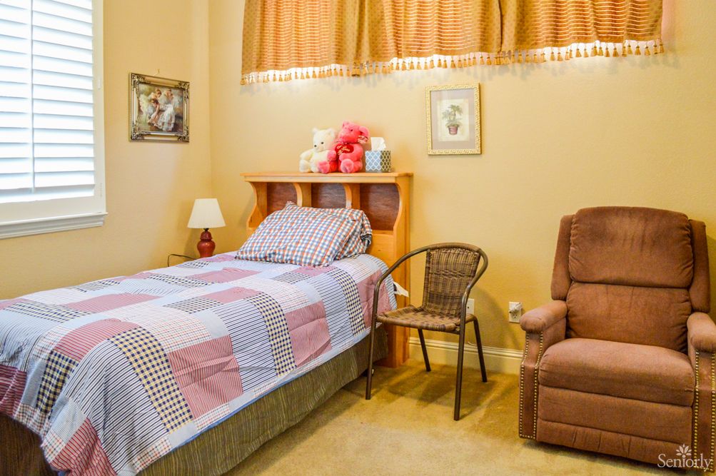 A cozy bedroom with a single bed, a brown armchair, and decorative items on the shelf.