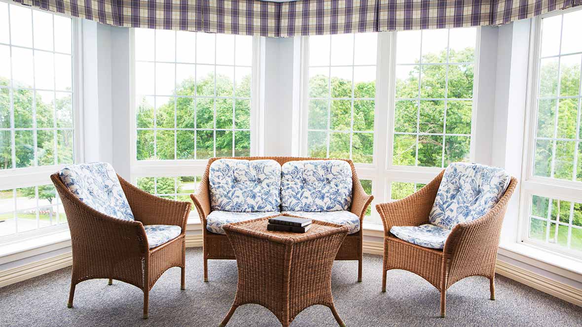 A bright sunroom featuring wicker furniture with floral-patterned cushions and large windows letting in natural light.