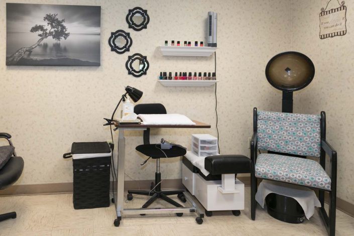 A manicure station in a nail salon, featuring a table with a lamp and an array of nail polish bottles on shelves.