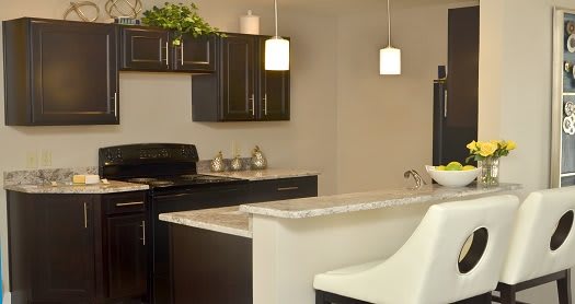 A modern kitchen with dark cabinets and a light countertop, featuring pendant lights and a bar stool.