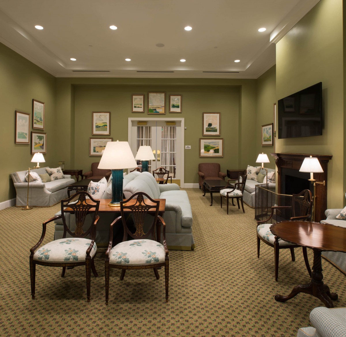 A traditional living room with elegant furniture, including sofas and chairs, softly illuminated by table lamps against a backdrop of framed artwork.