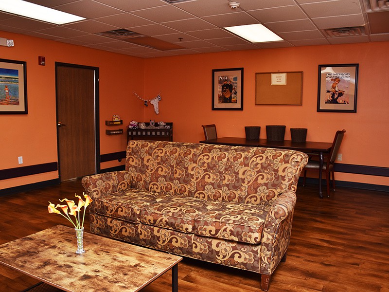 A cozy living room with an orange color scheme featuring a patterned couch, coffee table, and a dining area in the background.