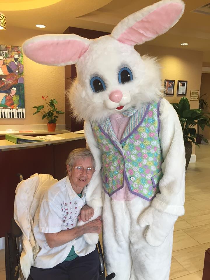 An elderly person posing with someone dressed as the Easter Bunny indoors.