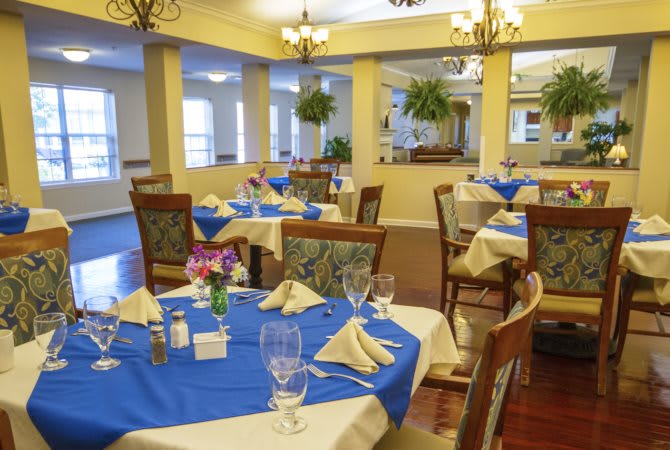 A well-decorated dining room with tables set with blue and white tablecloths, elegant napkins, and chairs around each table.