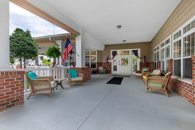 A welcoming porch area with comfortable seating and plants, featuring an American flag.