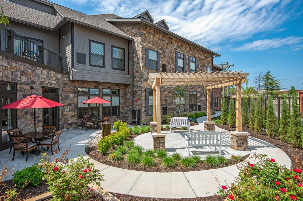 A beautifully landscaped backyard with a pergola and outdoor seating area, adjacent to a residential building.