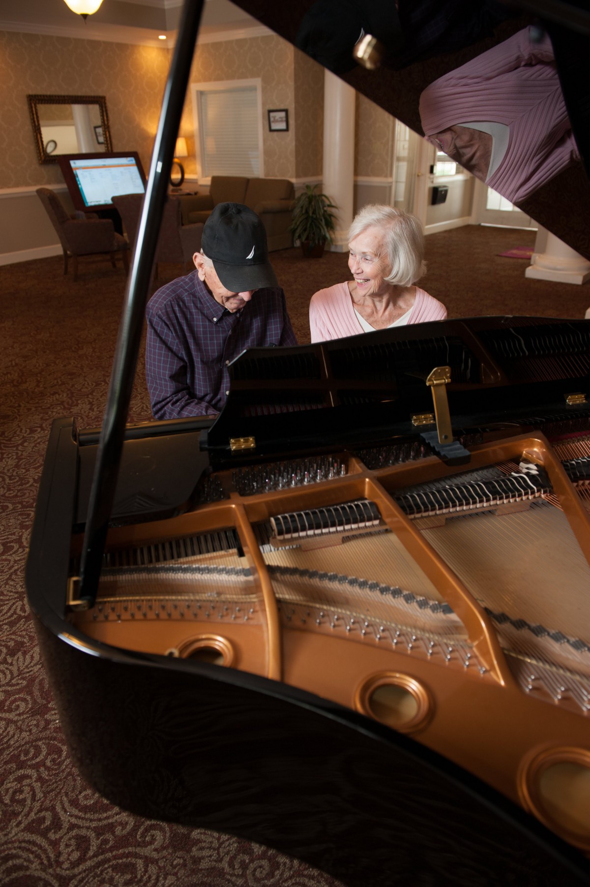 Two elderly individuals sitting at a grand piano, engaging in conversation.