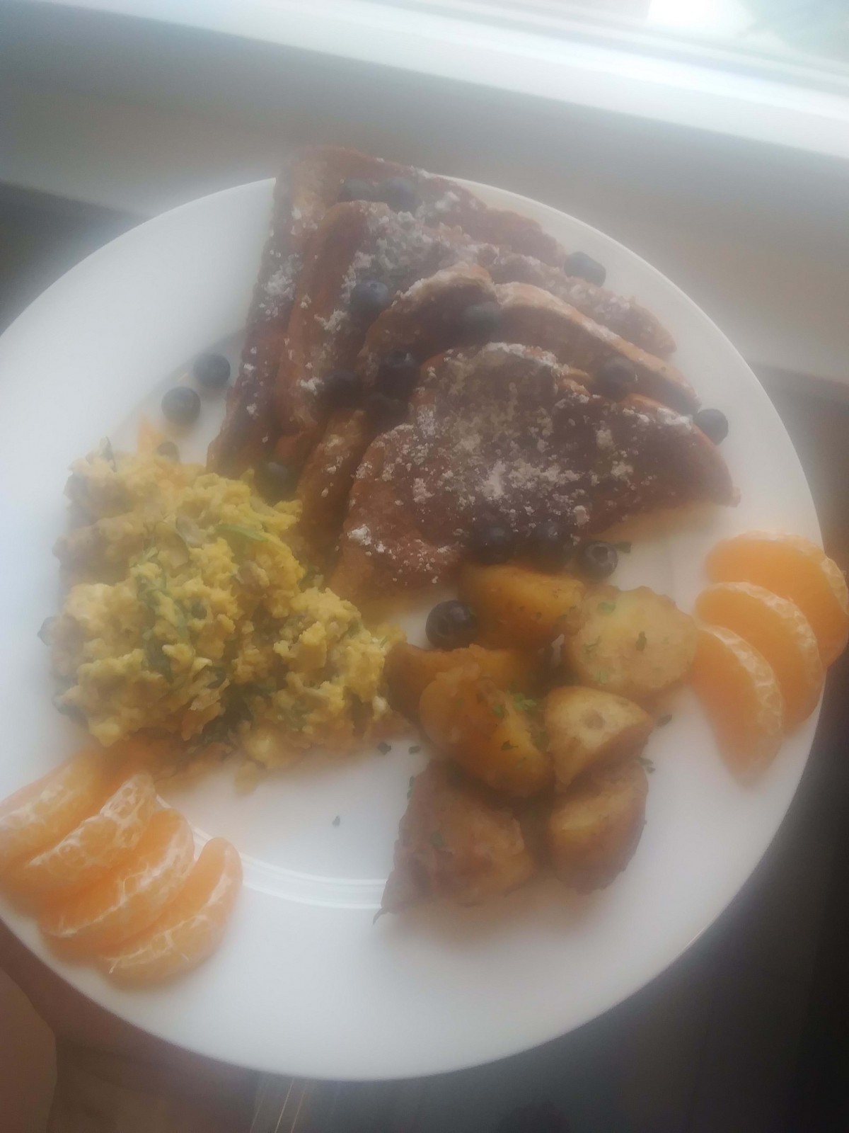 A plate with a meal consisting of meat, potatoes, scrambled eggs, and orange slices.