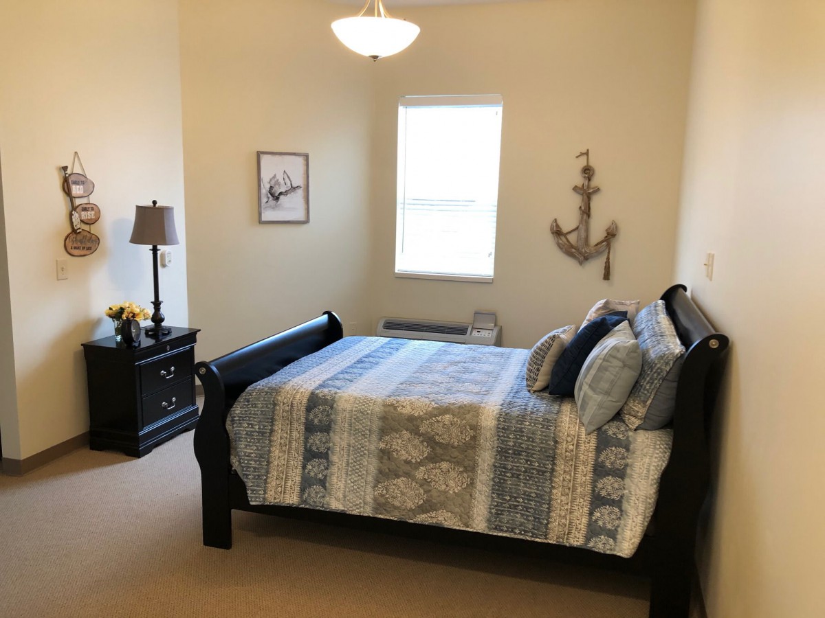 A cozy bedroom with nautical-themed decor, featuring a double bed, nightstand with a lamp, and an anchor wall hanging.