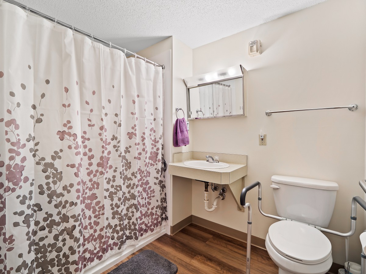 A well-lit bathroom featuring a shower with a patterned curtain, an accessible sink, and a toilet.