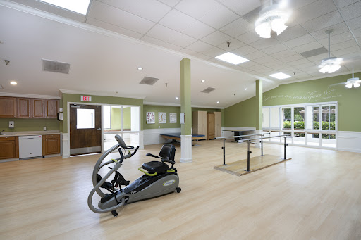 A bright and spacious rehabilitation gym featuring an elliptical machine and parallel bars for physical therapy.