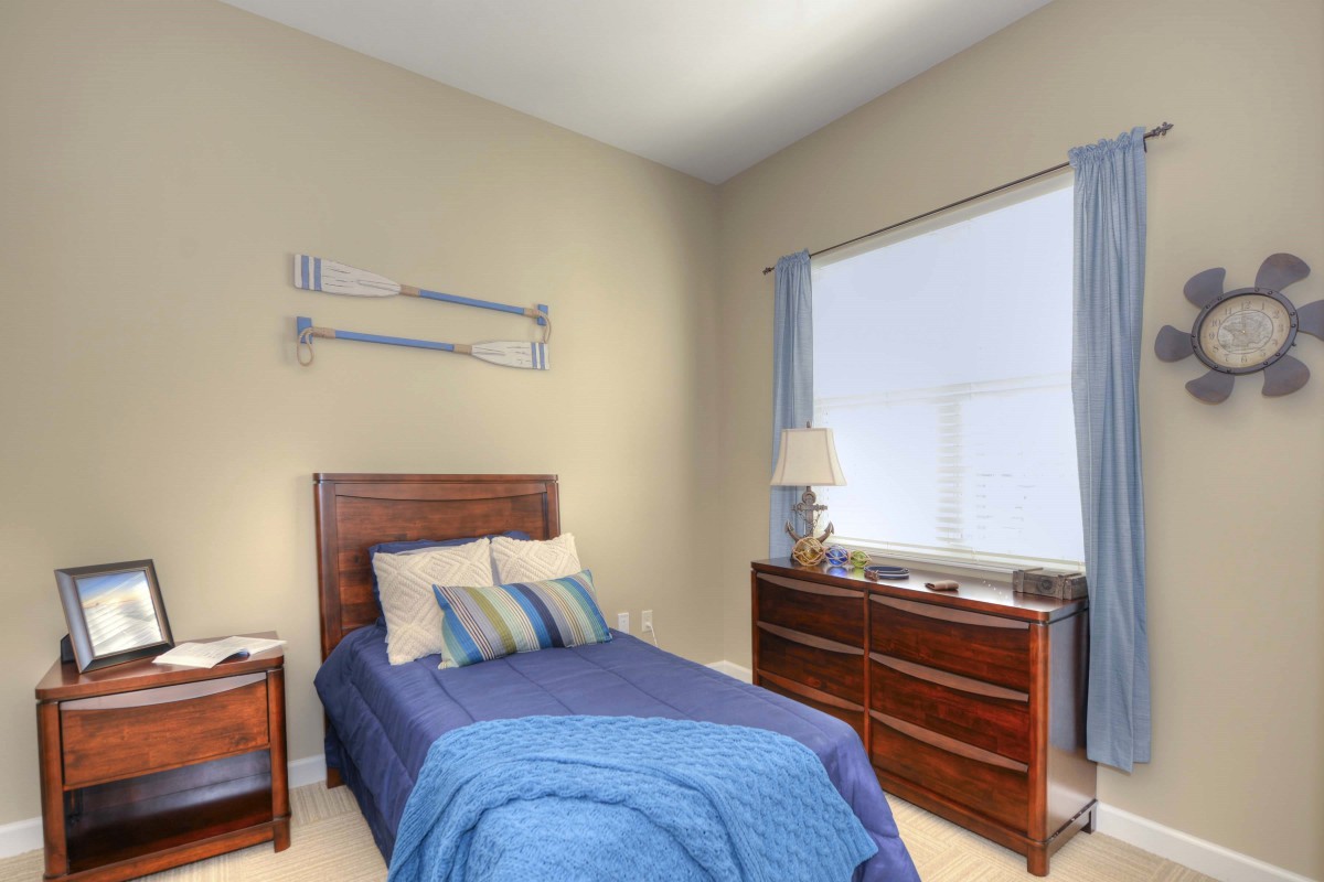 A cozy bedroom with a single bed, wooden dresser, and blue-themed decor.
