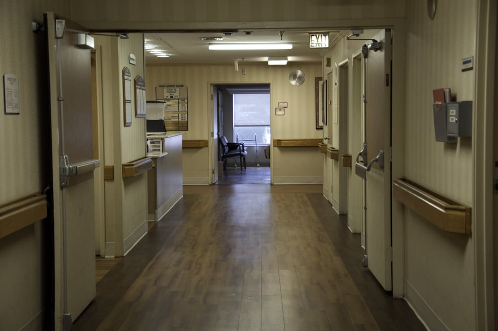An empty hospital hallway with multiple doors and a window at the end.