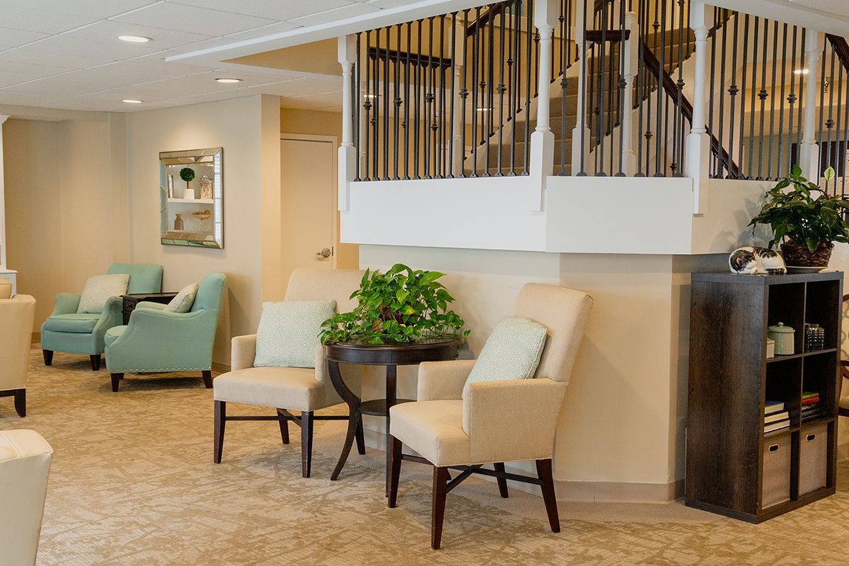 A cozy lobby interior featuring comfortable chairs, a side table with a plant, and a staircase.