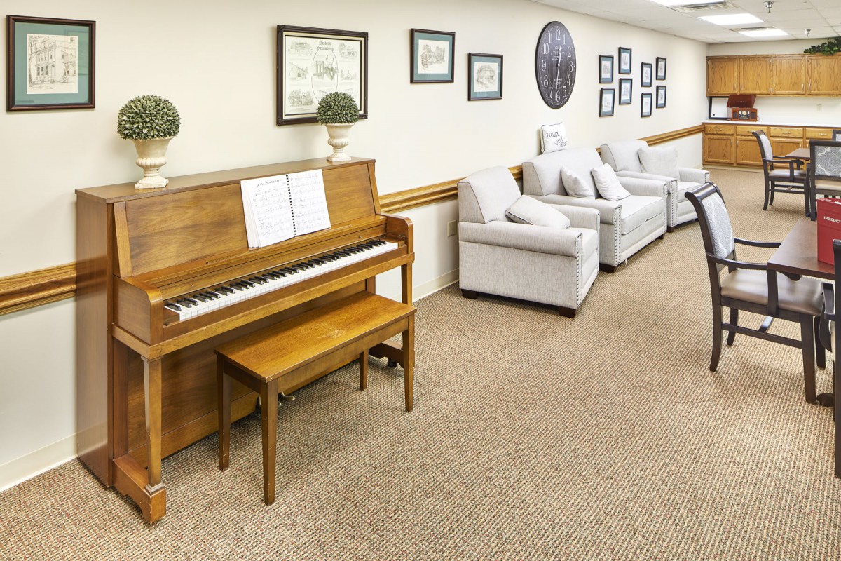 A cozy living room featuring a wooden piano and a comfortable sofa, decorated with framed artwork on the walls.