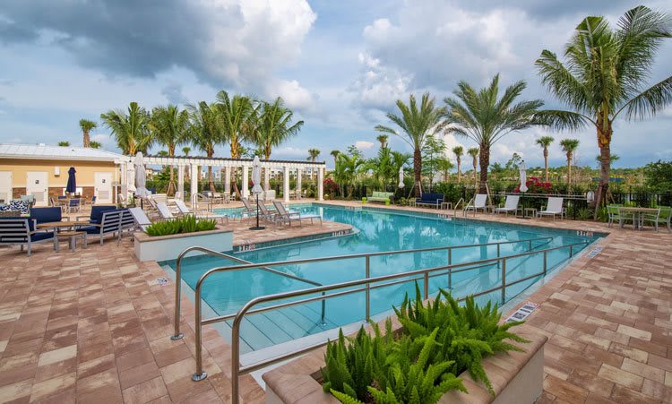 A serene outdoor swimming pool area surrounded by palm trees and lush greenery under a cloudy sky.