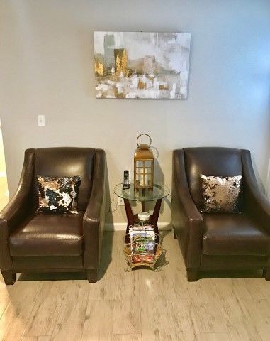 A cozy seating area with two leather chairs, decorative pillows, a small side table, and artwork on the wall.