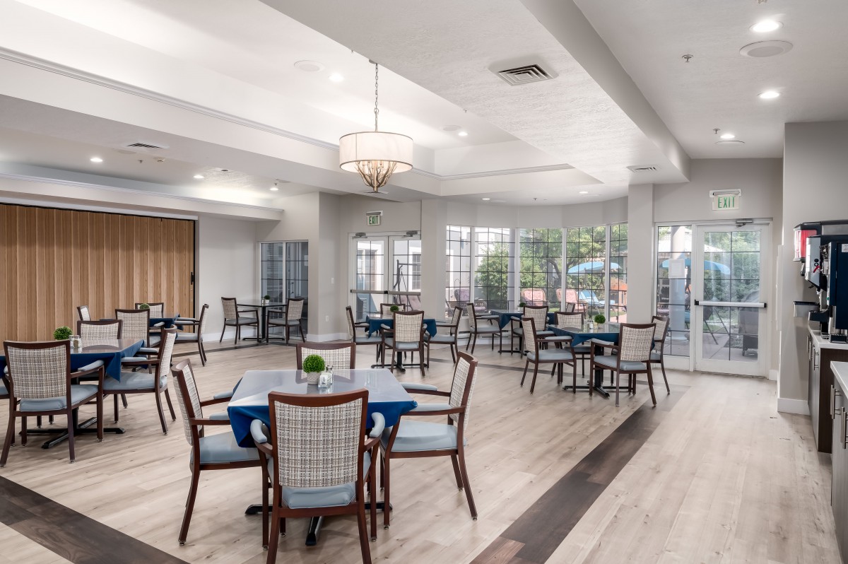 A spacious and well-lit dining room featuring multiple tables and chairs, with large windows allowing natural light to brighten the space.