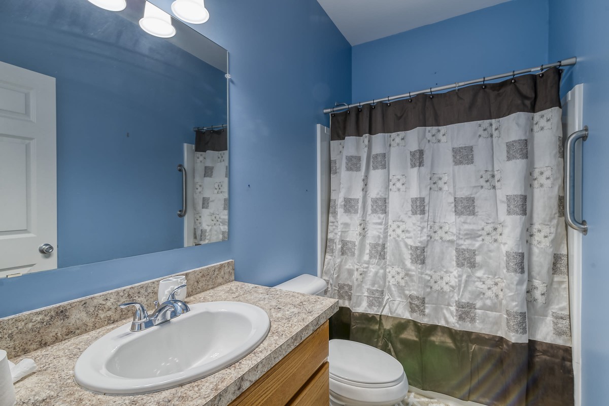 A modern bathroom with blue walls, featuring a sink, mirror, and a shower curtain.