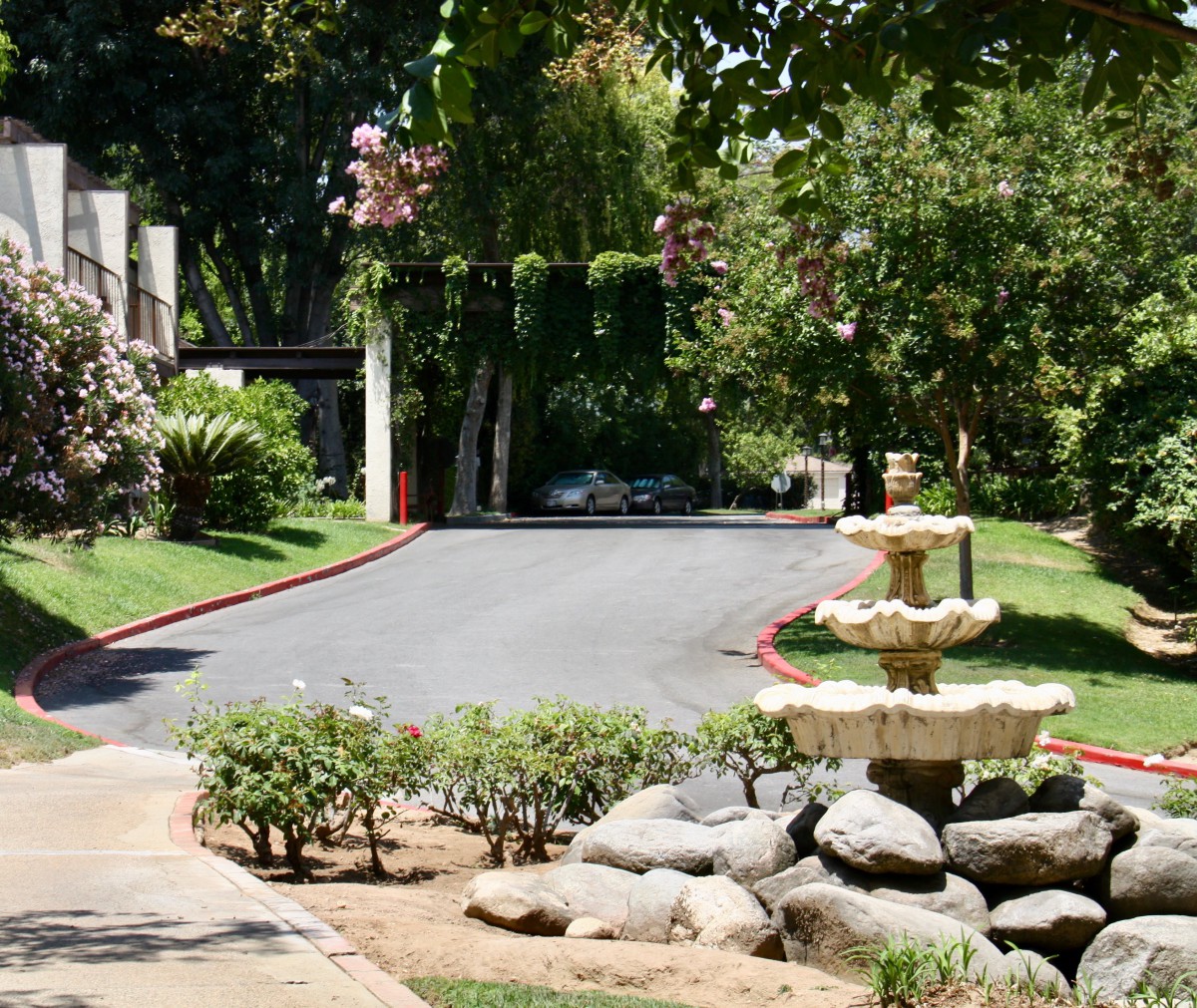 A serene garden with a stone fountain and lush pathway surrounded by greenery.