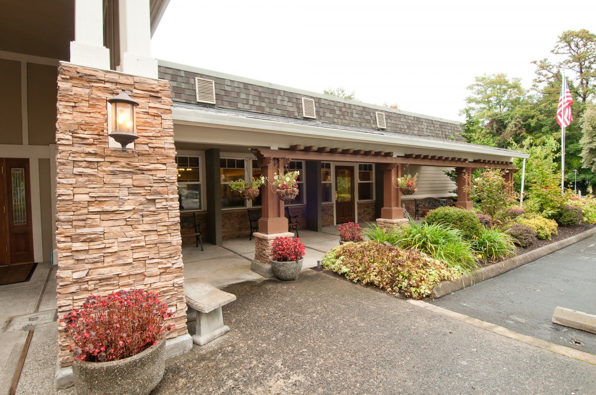 The image shows the exterior entrance of a building with landscaping and pavement.