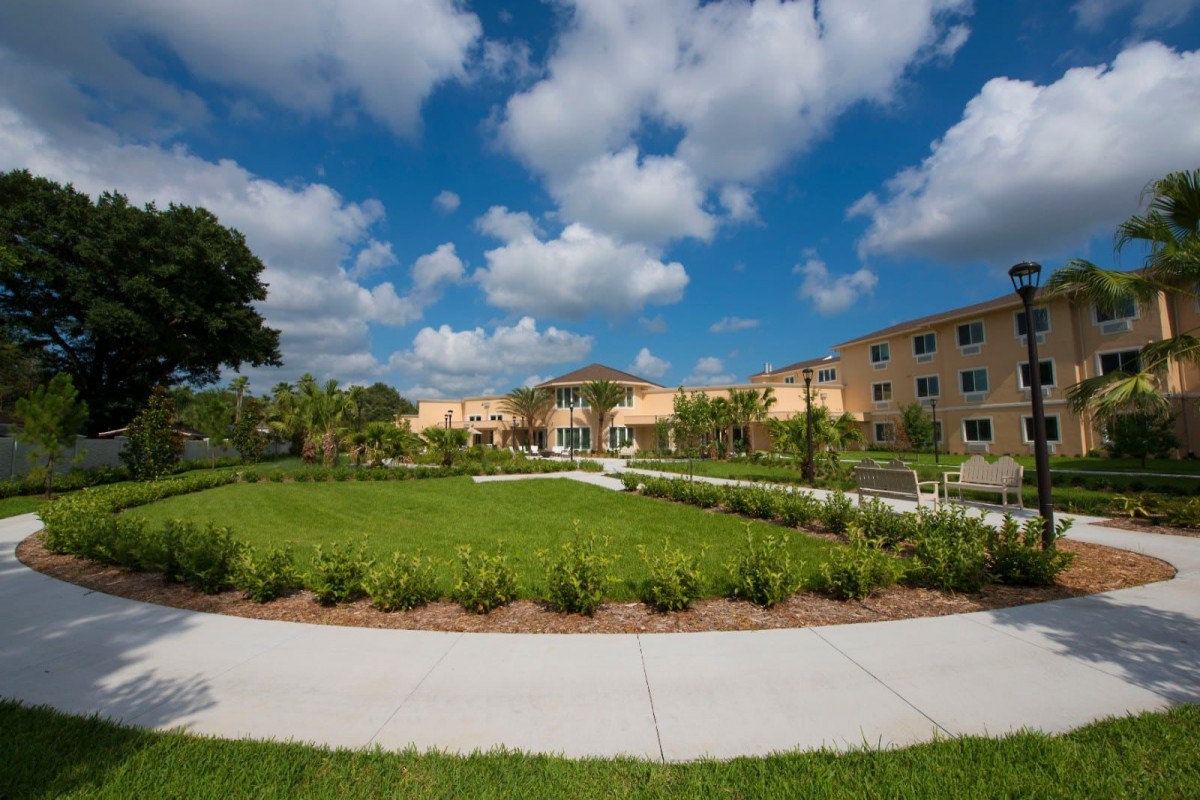 A well-maintained garden with a pathway, surrounded by a modern building under a partly cloudy sky.