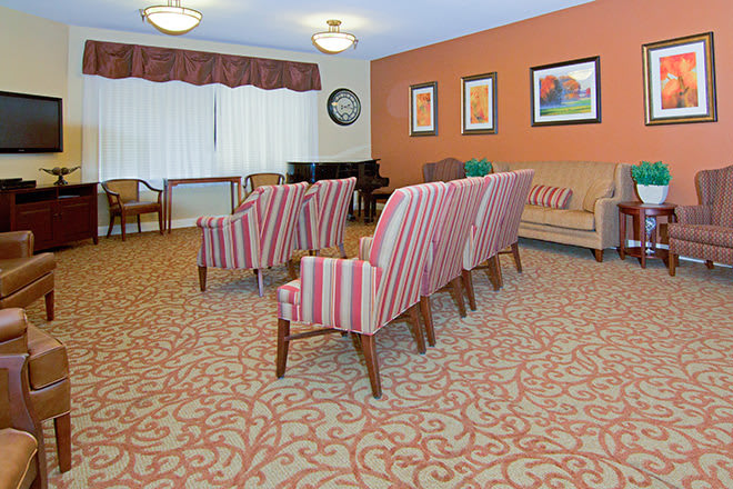 A cozy living room with striped chairs, a sofa, patterned carpet, and framed artwork on the walls.