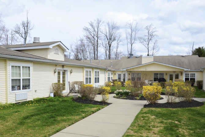 A view of a residential house with a well-maintained yard and pathway, surrounded by trees.