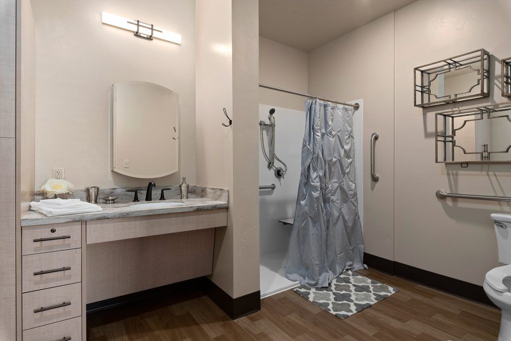 A modern bathroom featuring a shower with a curtain, a sink with a mirror, and wood-patterned flooring.