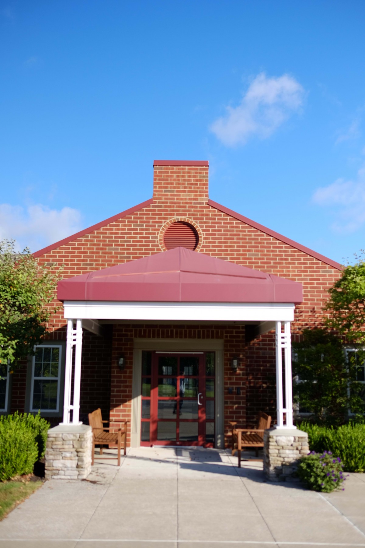A brick building with a covered entrance and red roof under a clear blue sky.