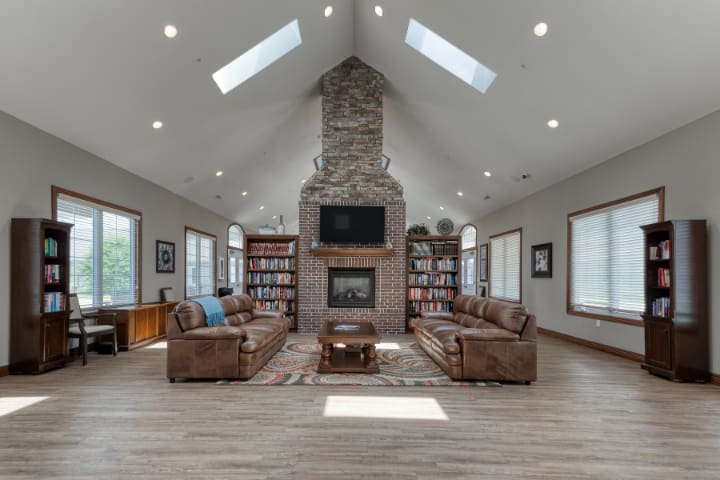 A spacious living room featuring a stone fireplace, comfortable sofas, built-in bookshelves, and natural light from skylights.
