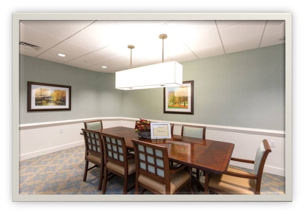 A well-lit dining room with a rectangular table and eight chairs, adorned with framed artwork on the walls.